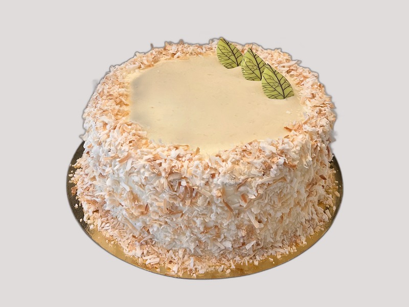 Whole banana coconut cake covered in toasted coconut flakes with pale green chocolate leaves