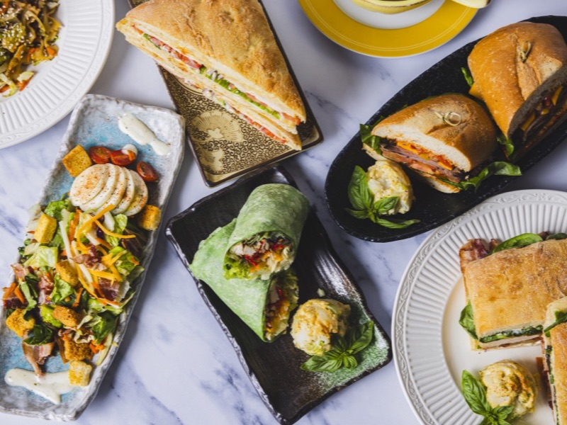 A table spread of Flower Flour sandwiches, wraps, salads, and a cup of soup