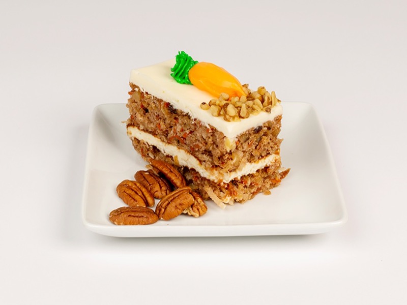 A slice of carrot cake with cream cheese frosting and a piped carrot
