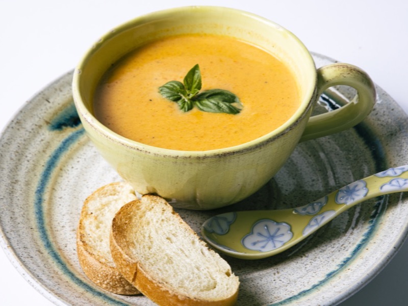 A cup of smooth orange soup with a basil leaf and toasted bread