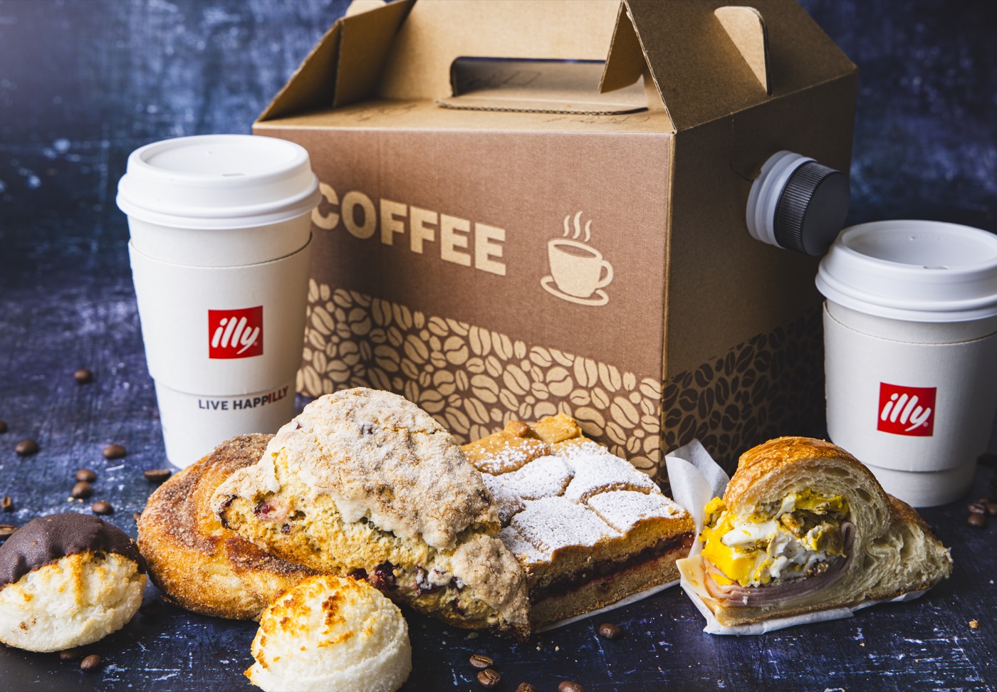 Two illy coffee cups beside a coffee box and an assortment of pastries